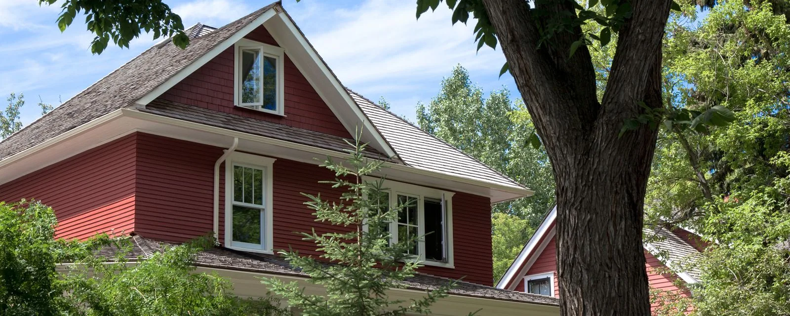 A red early-1900s character home under a mature elm in central Edmonton