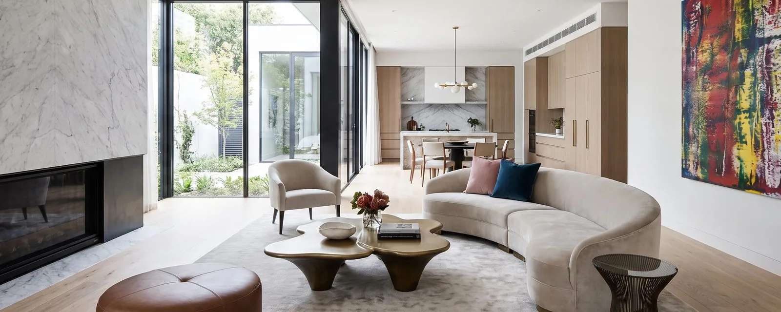 Open-plan living room with a full-height marble fireplace, a curved sofa and floor-to-ceiling glass onto a planted courtyard